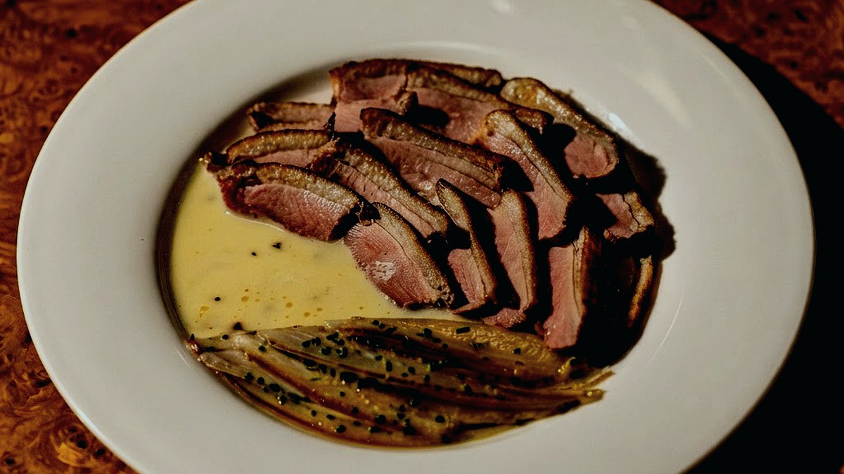 Pato servido com molho verde em prato de restaurante.
